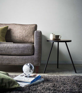 Profile view of Black Side Table by Yamazaki Home next to a sofa, holding a cup and a saucer. view 10