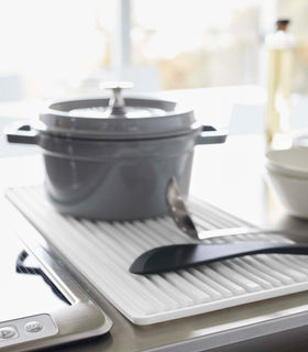 Close up of white Yamazaki Roll-Up Dish Drying Mat next to a kitchen stove with a dutch oven and utensils on top view 6