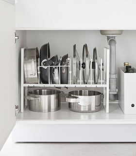 Front view of white Yamazaki Home Adjustable Pots and Pans Organizer underneath a sink storing pots and lids view 3