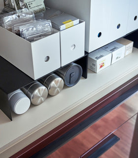 Close up of black Yamazaki Home Shelf Risers in a cabinet storing water bottles and food wrap boxes view 10