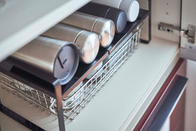 Close up view of black Expandable Countertop Organizer holding bottles in cabinet by Yamazaki Home. view 12