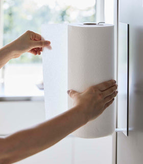 Side view of person grabbing paper towel from White Magnetic Paper Towel Holder by Yamazaki Home. view 6