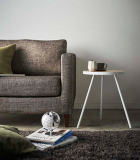 Profile view of White Side Table by Yamazaki Home next to a sofa, holding a cup and a saucer. view 4