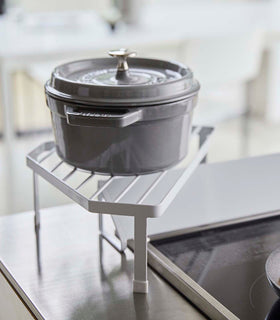 Side view of White Corner Riser holding pot next to kitchen stovetop by Yamazaki Home. view 4