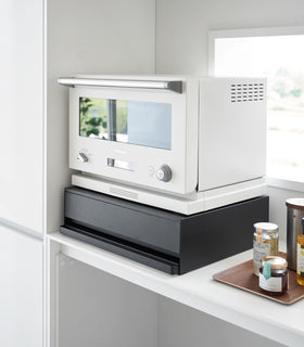 Diagonal view of the Countertop Drawer with Pull-Out Shelf by Yamazaki Home in black with the drawer and shelf tucked in. A small microwave sits atop the unit. view 11