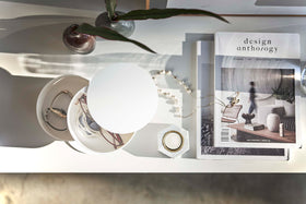 A bird’s-eye view of a two-tier white swivel accessory holder on a white dresser. Two decorative vases are seen behind the accessory holder and to the right of it are a stack of design books and a strewn pearl necklace.  Sunlight is casting a shadow from the right. view 7