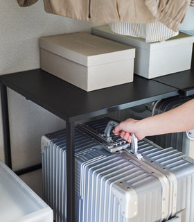 Close up of a suitcase being removed from underneath a black Yamazaki Home Expandable Suitcase Rack view 16