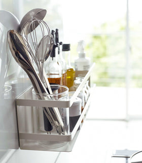 Side view of white Magnetic Storage Basket holding kitchen utensils, spices, and oils by Yamazaki Home. view 3