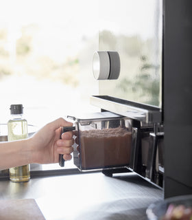 Image showing a hand lifting the front panel of the Concealable Spice Rack by Yamazaki Home in black by the handle, revealing various condiments inside. view 14