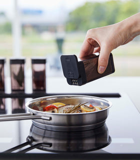 Black Yamazaki Home Spice Jar being used to season food in a pan view 14