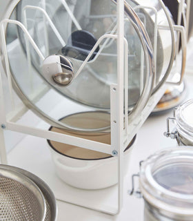 Close up of white Yamazaki Home Adjustable Pots and Pans Organizer underneath a sink storing pot lids view 8