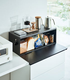 Side view of black Yamazaki Home Bread Box - Wide open on a counter with bread and snacks inside view 9