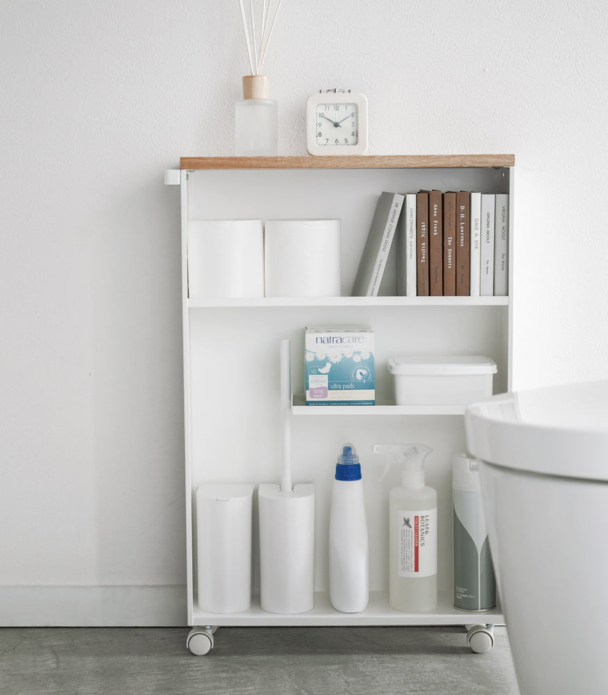 View 4 - Front view of white Rolling Storage Cart displaying cleaning supplies, toilet paper, and books in bathroom by Yamazaki Home.