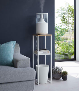 Pedestal Stand in white by Yamazaki Home in a living room holding a humidifier, some books, and a waste bin on the bottom. view 2