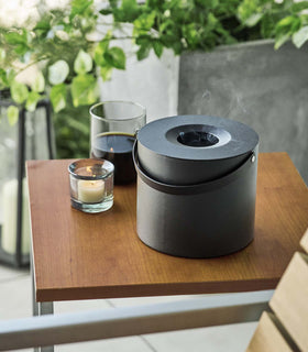 Black Yamazaki Mosquito Repellant Coil Holder and Storage Case lit on a table outside beside a candle view 5