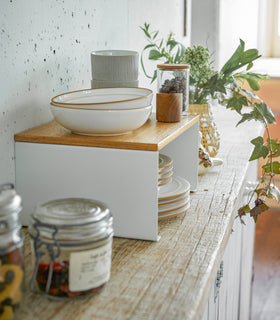 Side view of white Stackable Countertop Shelf on kitchen shelf holding bowls and cups by Yamazaki Home. view 11