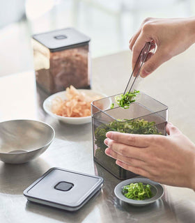 Person using tongs to grab scallions out of black Vacuum-Sealing Food Container on kitchen countertop by Yamazaki Home. view 24