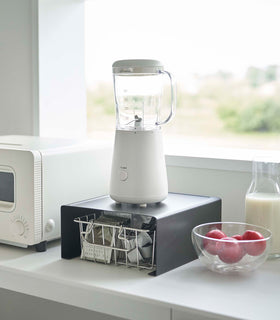 Black Yamazaki Home Stackable Countertop Shelf with a blender above and a basket of tea underneath view 12