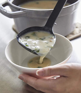 Close up view of black Floating Ladle serving soup into bowl by Yamazaki Home. view 4