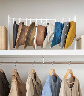 Frontal view of white Yamazaki Home hat rack hanging a variety of hats in a closet view 5