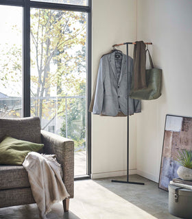 Yamazaki black Corner Leaning Coat Hanger in a the corner of a room with clothing hung on it view 10