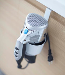 Close up view of white Blow Dryer Holder holding blow dryer on bathroom cabinet by Yamazaki Home. view 3