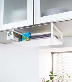 White Undershelf Organizer hanging from cabinet holding storage items and towels by Yamazaki Home. view 2