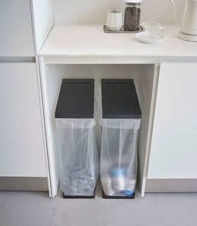 Two Black Yamazaki Home Lidded Garbage Bag Holder under a shelf view 13