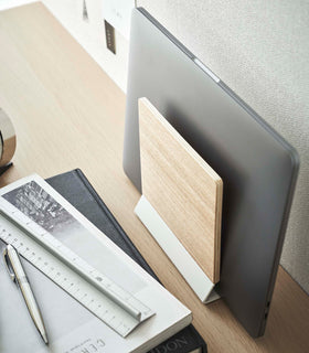 A side-view profile of a narrow wooden stand with a white metal base positioned by books on top of a desk. view 5