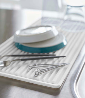 Close up of white Yamazaki Roll-Up Dish Drying Mat next to a kitchen sink with dishes drying on top view 5