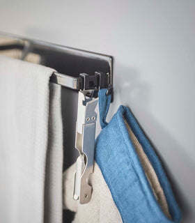 Close up view of black Magnetic Kitchen Towel  with hooks holding bottle opener, oven mitt, and towel by Yamazaki Home. view 13