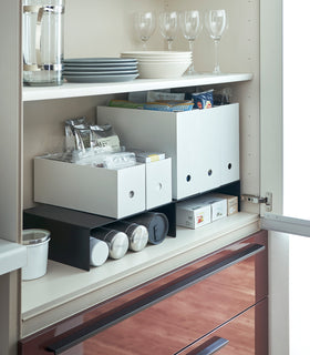 Black Yamazaki Home Shelf Risers in a cabinet storing water bottles and wrap boxes beneath view 8