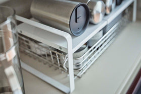 Close up view of white Expandable Countertop Organizer holding bottles in cabinet by Yamazaki Home. view 6