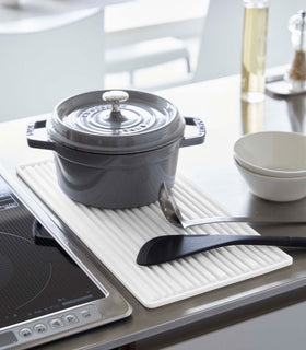 White Yamazaki Roll-Up Dish Drying Mat next to a kitchen stove with a dutch oven and utensils on top view 3