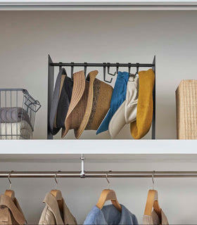 Frontal view of shortened black Yamazaki Home hat rack hanging a variety of hats in a closet view 16