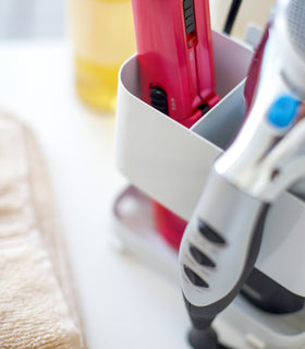 Closeup view of white Haircare Appliance Holder holding blow dryer and straightener by Yamazaki Home. view 4