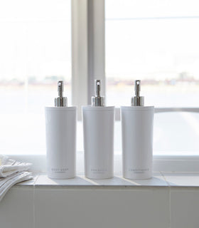 Front view of Yamazaki Home white Shampoo, Conditioner, and Body Soap dispensers in bathroom. view 3