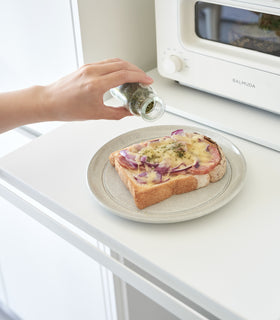 Close-up image of a hand seasoning food on a plate placed on the pulled out shelf of the Countertop Drawer with Pull-Out Shelf by Yamazaki Home in white. view 7