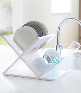 Side view of white X-Shaped Dish Rack holding dinnerware by Yamazaki Home. view 3