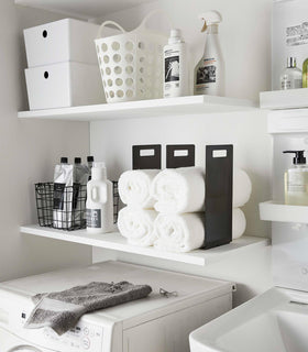 Black Towel Storage Organizer holding towels on laundry room shelf by Yamazaki Home. view 10