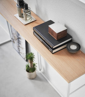 Diagonal, close-up view of the Long Console Table by Yamazaki Home in white placed by a wall with decorative items. view 5