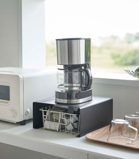 Black Yamazaki Home Stackable Countertop Shelf with a coffee pot above and a basket of tea underneath view 11