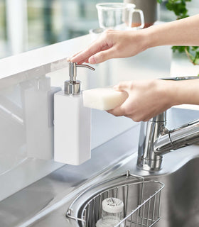 Dispensing soap from white Yamazaki Home square soap dispenser onto dish sponge view 3