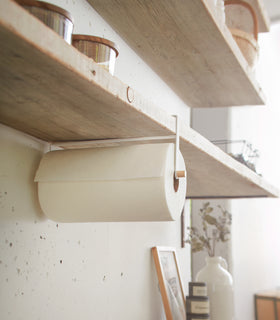 Side view of white Udnershelf Organizer holding paper towel on kitchen shelf by Yamazaki Home. view 3