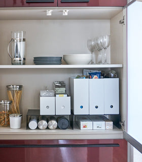 Front view of black Yamazaki Home Shelf Risers in a cabinet storing water bottles and wrap boxes view 9