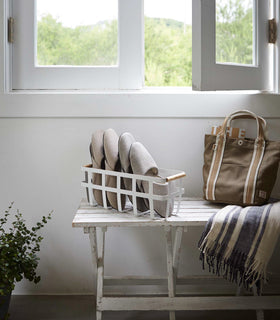 White Storage Basket containing slippers on bench by Yamazaki Home. view 3