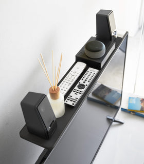 Aerial view of black Compliant TV Shelf holding speakers and remotes in living room by Yamazaki Home. view 7