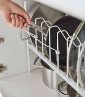 A pan being pulled from a white Yamazaki Home Adjustable Pots and Pans Organizer view 5