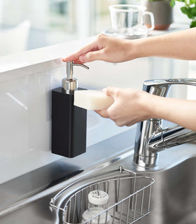 Dispensing soap from black Yamazaki Home square soap dispenser onto dish sponge view 10