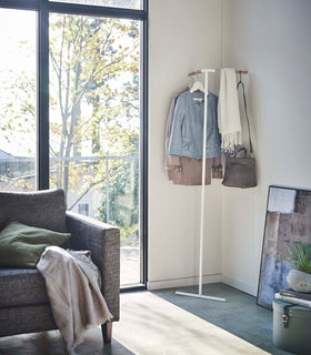 Yamazaki white Corner Leaning Coat Hanger placed in the corner of a room with items hung on it view 2